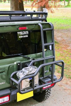 the back end of a green jeep parked in front of a tree and grass field