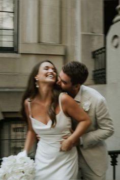 a bride and groom kissing in front of a building