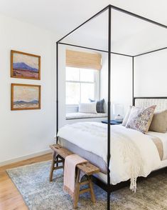 a bedroom with a four poster bed and white walls, hardwood flooring and artwork on the wall