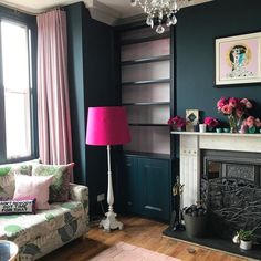 a living room filled with furniture and a pink lamp next to a fire place in front of a window