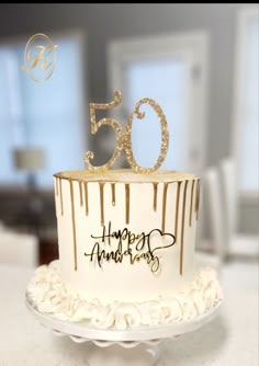 a white and gold cake with the number 50 on it's top is sitting on a table