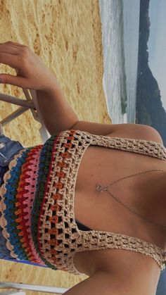 a woman in a multicolored crochet bathing suit sitting on a beach chair