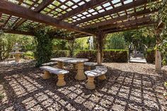 an outdoor picnic area with several benches and tables in the shade under a pergolated roof