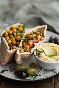 two pita sandwiches on a plate with hummus and olives