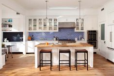 a kitchen with wooden floors and white cabinets, an island in the middle is surrounded by four stools