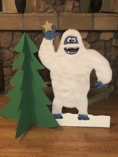 a paper cut out of a monster standing next to a christmas tree