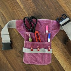 a pair of scissors and some other items in a pink bag on a wooden floor