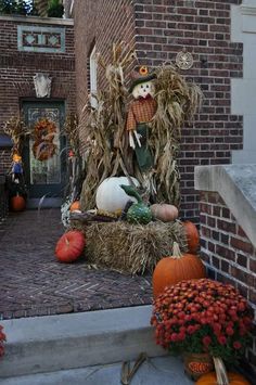 pumpkins and gourds in front of a brick building with scarecrow decorations