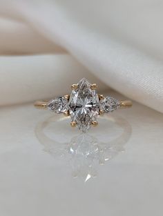 an engagement ring with three pear shaped diamonds on the side, sitting on a white cloth