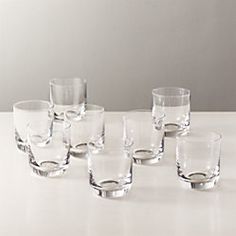 several clear glasses are lined up on a white counter top, with one empty glass in the middle