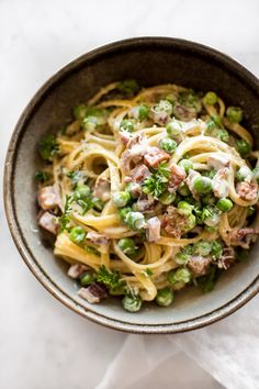 a bowl filled with pasta and peas on top of a white table next to a napkin