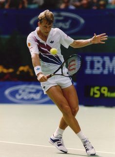 a man hitting a tennis ball with a racquet on a court while people watch from the stands