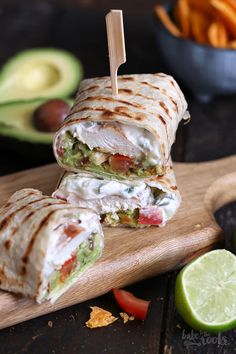 a cut in half sandwich sitting on top of a cutting board next to sliced avocado