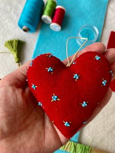 a hand holding a red heart shaped ornament with spools of thread in the background