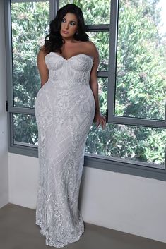 a woman standing in front of a window wearing a white dress and posing for the camera