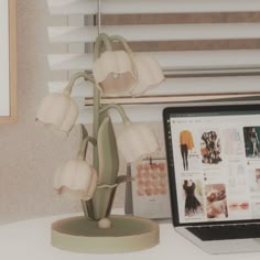 a laptop computer sitting on top of a desk next to a vase with flowers in it