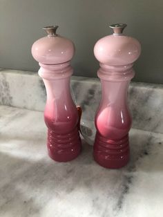 two pink salt and pepper shakers sitting on top of a marble counter next to each other