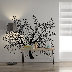 a living room with a table, lamp and tree wall decal