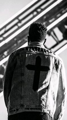 a man wearing a jean jacket with a cross painted on the back of his jacket