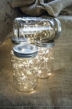 two mason jars sitting on top of a burlock covered tablecloth with lights in them