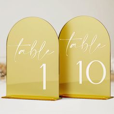 two gold table numbers with white calligraphy on the front and back of each one