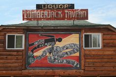 a wooden building with a large sign on top of it that says lumber tavern and an image of a snake painted on the side