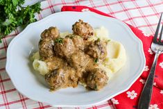 a white plate topped with meatballs and mashed potatoes on top of a red checkered table cloth