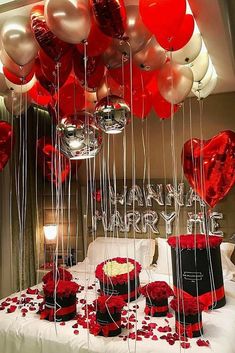 red and white balloons are hanging from the ceiling in front of a bed with hearts on it