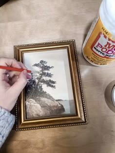 a person is holding a pencil and painting a picture on a table with other items