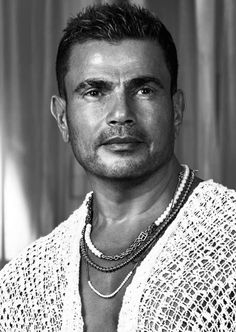 a black and white photo of a man with necklaces on his neck looking at the camera