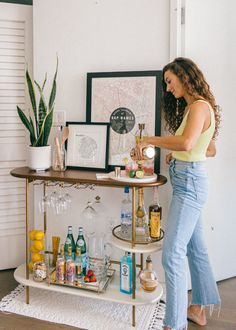 a woman standing in front of a bar cart filled with liquor bottles and alcohol glasses