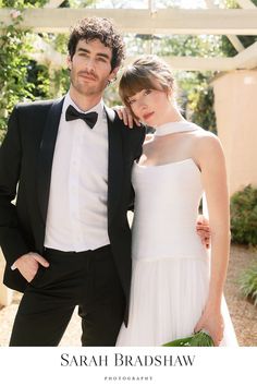 a man in a tuxedo and a woman in a white dress pose for a photo