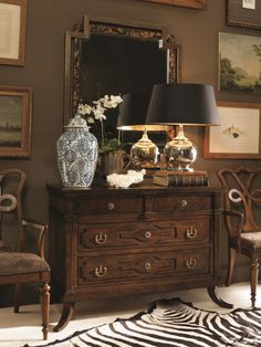 a dresser with two vases and a lamp on it in a room filled with pictures