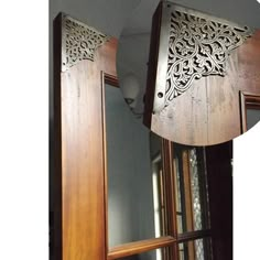 an intricately carved wooden mirror hanging from the side of a wall in front of a window