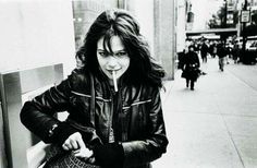 a black and white photo of a woman leaning against a wall with her finger in her mouth