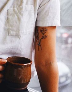 a person with a flower tattoo on their arm holding a coffee mug in front of a window