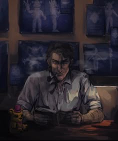 a man sitting at a table with a book in front of him and some pictures on the wall behind him