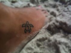 a small tattoo on the foot of a person laying in the sand at the beach