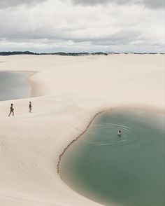 two people are walking in the sand near some water and white sand with blue skies