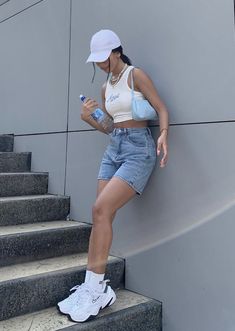 a woman leaning up against a wall while looking at her cell phone and drinking water