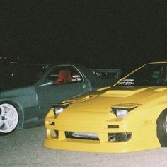 two cars parked next to each other in a parking lot at night with one car on the ground