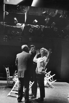 two men and a woman standing in front of a stage with lots of chairs on it