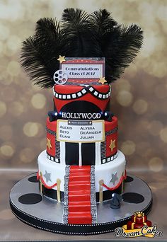 a three tiered cake decorated with black feathers and hollywood memorabilia is displayed on a table