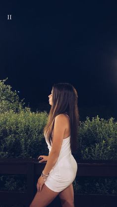 a woman in a short white dress is walking down the street at night with her hand on her hip