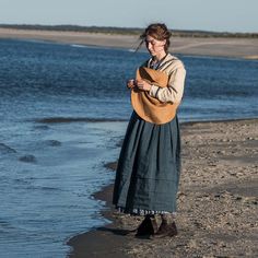 a woman is standing on the beach and looking at her cell phone while wearing an apron