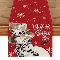 a snowman wearing a hat and scarf on top of a wooden board with the words let it snow