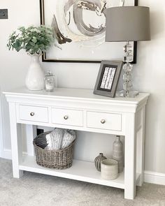 a white console table with two baskets and a lamp on top, in front of a painting