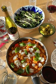 a table topped with plates and bowls filled with food next to bottles of wine on top of a wooden table