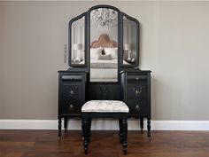 a black vanity with mirror and stool in front of it on hard wood flooring