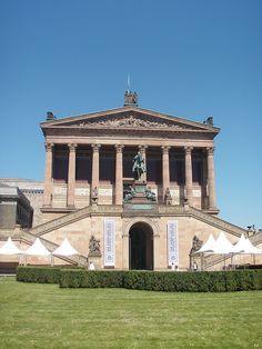 a large building with columns and pillars on the top floor, surrounded by green grass